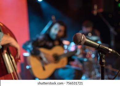 Acoustic Trio Band Performing On A Stage In A Nightclub, With The Microphone In Focus Waiting For Its Singer