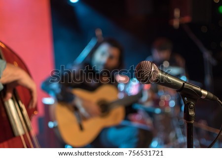 Acoustic trio band performing on a stage in a nightclub, with the microphone in focus waiting for its singer