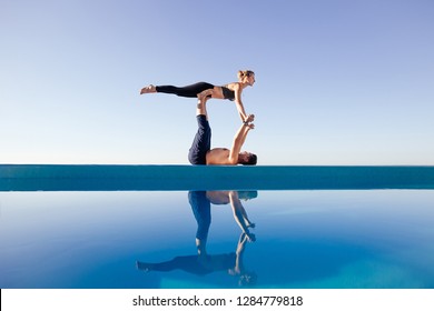 Acro yoga concept. Pair yoga. Couple of young sporty people practicing yoga lesson with partner, man and woman in yogi exercise, arm balance pose, working out by pool, above beach, against blue sky - Powered by Shutterstock