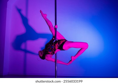 Acrobatic pole dance. Grace and strength, professional dancer. A woman is practicing gymnastics on a pole in the neon light of the studio. - Powered by Shutterstock