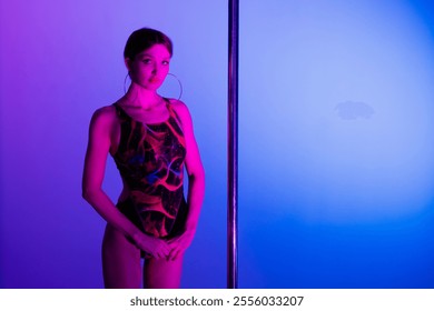 Acrobatic pole dance. Grace and strength, professional dancer. A woman is practicing gymnastics on a pole in the neon light of the studio. - Powered by Shutterstock