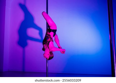 Acrobatic pole dance. Grace and strength, professional dancer. A woman is practicing gymnastics on a pole in the neon light of the studio. - Powered by Shutterstock