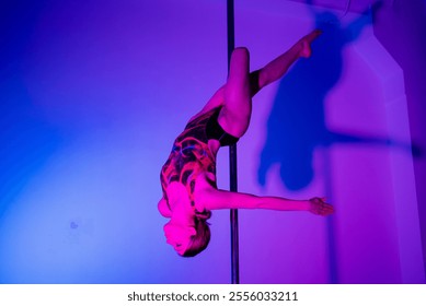 Acrobatic pole dance. Grace and strength, professional dancer. A woman is practicing gymnastics on a pole in the neon light of the studio. - Powered by Shutterstock