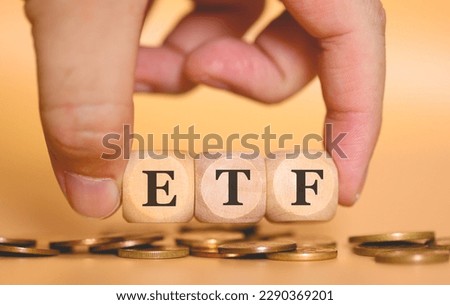 The acronym ETF for Exchange Traded Fund written on wooden dice a man is holding. Studio shot with orange background and coins in the composition.
