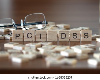 the acronym PCI DSS for Payment Card Industry Data Security Standard concept represented by wooden letter tiles on a wooden table with glasses and a book
