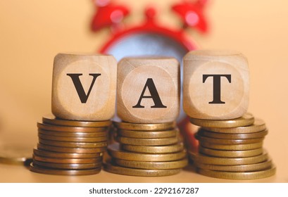 The acronym VAT for Value-Added Tax written on wooden dice lying on top of piles of coins. Studio photo. An alarm clock in the composition.
 - Powered by Shutterstock