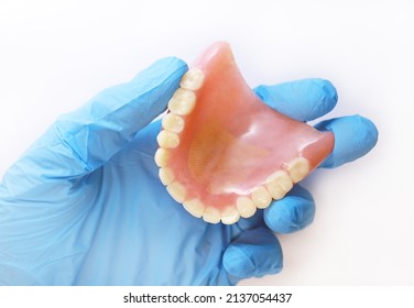 An acrylic denture in a gloved hand. Doctor's hand holds a denture. Set of false teeth. - Shutterstock ID 2137054437