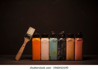 Acrylic Paint Bottles Set And Paintbrush On Dark Background. Copy Space.