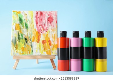 Acrylic paints of different colors and small easel with abstract picture on light blue background - Powered by Shutterstock