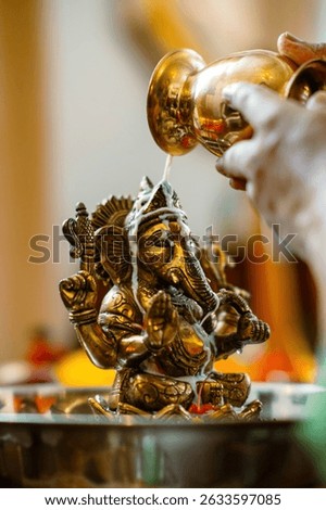 Act of devotion captured. Milk streams from golden pot onto detailed Ganesha idol's head in a religious offering. Use for world religions or spiritual practices materials.