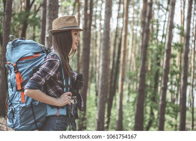 Action adventure. Side view profile of pleasant optimistic young woman wearing hat is standing in forest with rucksack and binoculars. She is looking ahead with slight smile. Copy space in right side - Powered by Shutterstock