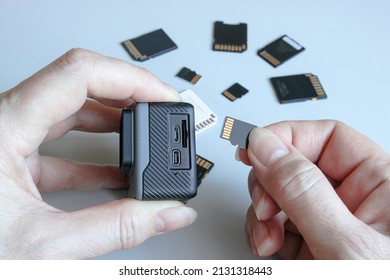 Action camera and microSD memory card in hands on the back of other SD memory cards. Background from gadgets and digital devices.