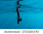 Action camera on a floating hand grip handle underwater in clear blue sea water with small fish on the background.