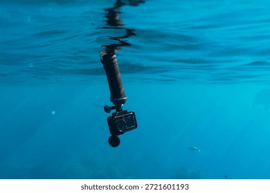 Action camera on a floating hand grip handle underwater in clear blue sea water with small fish on the background.