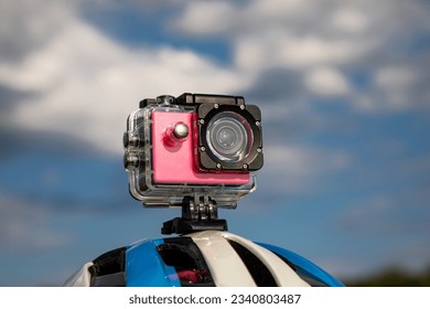 Action camera in a protective box on a bicycle helmet against a blue sky background.