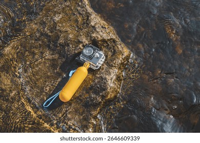 An action camera with a waterproof case and a float for swimming rests on a rock in the water