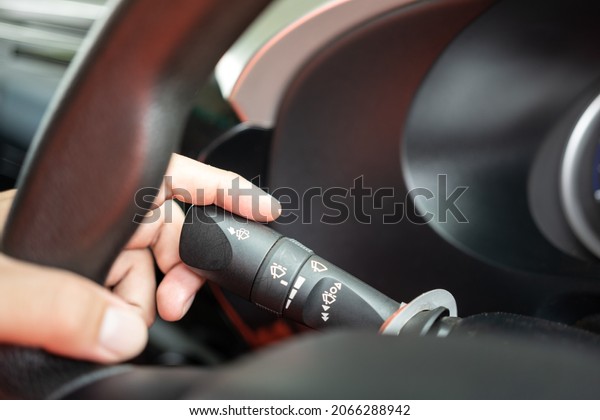 Action of a car driver is controlling lever\
switch to activate the rain wiper blade when driving in raining.\
Transportation technology photo. Close-up and selective focus on\
the driver\'s index\
finger.