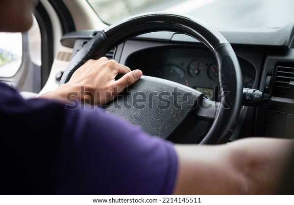 Action of a\
driver hand is holding and controlling on car\'s steering wheel\
during driving, photo from behind. Transportation occupation\
service with people part, selective\
focus.