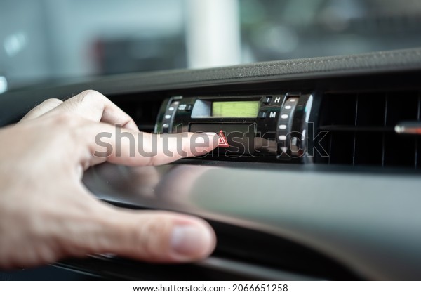 Action of driver is pressing on the emergency\
signal switch during accident or breakdown situation, calling for\
help. Transportation scene photo. Close-up and selective focus at\
the switch\'s part.