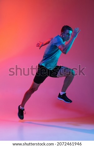In action, dynamic. Portrat of Caucasian male athlete, runner training isolated on pink studio background with blue neon filter, light. Concept of action, motion, speed, healthy lifestyle. Copyspace