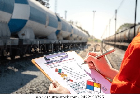 Action of an engineer is checking on chemical hazardous material checklist form with background of train freight tanker for crude oil or chemical cargo. Industrial safety working scene. 