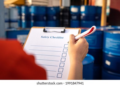 Action Of Factory Supervisor Is Using A Pen To Checking On Safety Checklist Form, With Blurred Background Of Chemical Storage Area. Close-up And Selective Focus At The Human Hand Part.