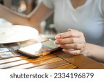 Action of human hand is playing mobile which is placed on wooden table during eating breakfast. Social addict concept, photo applied with oranage shade lighting, selective focus at human hand.