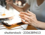 Action of human hand is playing mobile which is placed on wooden table during eating breakfast. Social addict concept, photo applied with oranage shade lighting, selective focus at human hand.