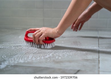 Action Of A Human's Hand Is Using Floor Brush To Cleaning Toilet Marble Tile Floor. Close-up And Selective Focus At Hand Part.