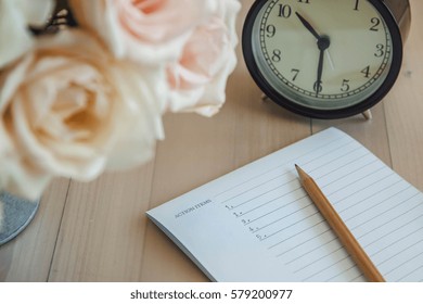 Action Items Write Down On Notebook By Pencil Put On Wooden Table With Black Vintage Clock And Vase Of Bouquet Rose.