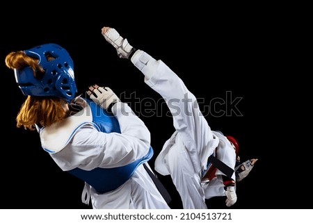 In action and motion. Dynamic portrait of two young women, taekwondo athletes training together isolated over dark background. Concept of extreme sport. Concept of sport, education, skills, workout