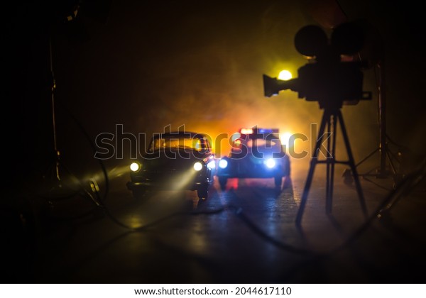 Action movie concept.\
Police cars and miniature movie set on dark toned background with\
fog. Police car chasing a car at night. Scene of crime accident.\
Selective focus