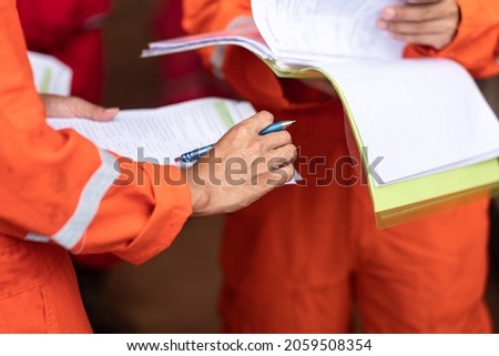 Action of operation supervisor is holding document paper during operational group meeting with other staffs. Industrial expertise occupation action photo. Close-up and selective focus at hand