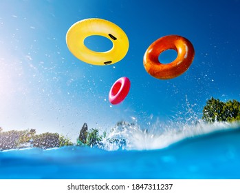 Action photo in the outdoor swimming pool with splashes and waves of inflatable doughnuts buoys rings falling down over sky