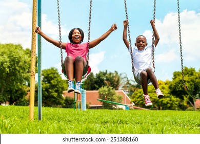 Action Portrait Of Shouting African Kids Playing On Swing In Neighborhood.Out Of Focus Houses In Background.