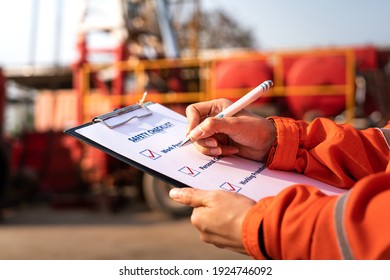 Action of safety office is writing on checklist paper during safety audit and risk verification at drilling site operation with blurred background of mount truck rig. Selective focus at hand.