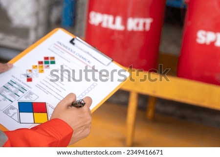 Action of safety officer is checking chemical hazard material form for correct the oil spill kit which is placed at front of chemical storage warehouse area in factory. Close-up and selective focus.
