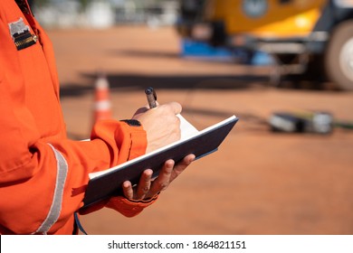 Action of safety officer is taking note on checklist with blurred background of crane truck vehicle. Safety inspection audit in heavy operation concept photo, selective focus at the person's hand.