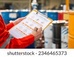 Action of safety officer is using a pen to checking on the hazadous material symbol label form with the chemical barrel as blurred background. Safety industrial working scene concept. Selective focus.