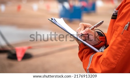 Action of safety officer is writing and check on checklist document during safety audit and inspection at drilling site operation. Industrial expertise occupation working scene.