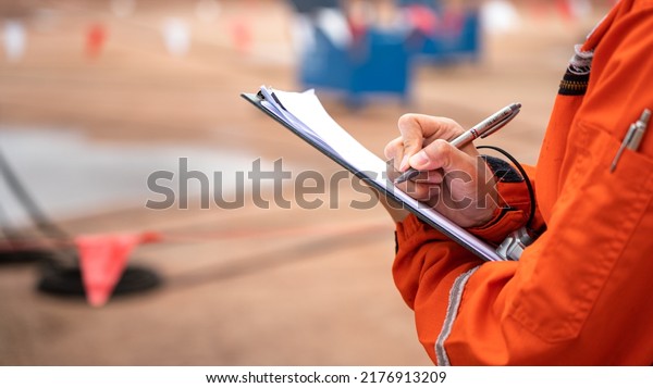 Action of safety\
officer is writing and check on checklist document during safety\
audit and inspection at drilling site operation. Industrial\
expertise occupation working\
scene.