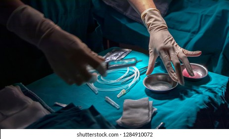 Action Of Scrub Nurse While She Prepare The Syringe And Instrument For Surgeon In Case Of Minor Operation. Close Up Photo With Dramatic Light From Surgical Lamp. Medical Concept With Dark Copy Space.
