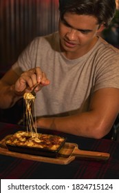 An Action Shoot Of A Young Handsome Man Is Enjoying His Food Using A Fork To Stretch Cheese From Macaroni And Cheese Or Mac N Cheese Meal In A Restaurant