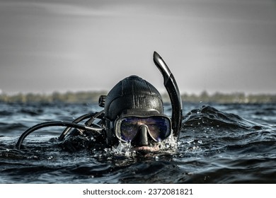 An action shot of a male scuba diver on the surface of the cold water about to descend on a dive. Grey clouds and serious expression  atmosphere and bubbles from exhalation give action