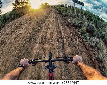 Action shot point of view from a mountain biker cycling down a gravel road towards the sunset. 