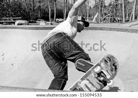 Action shot of a skateboarder skating in a concrete skateboarding bowl at the skate park. High contrast black and white.
