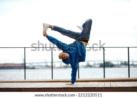 Action shot of young man doing breakdance stunt pose outdoors against sky, copy space
