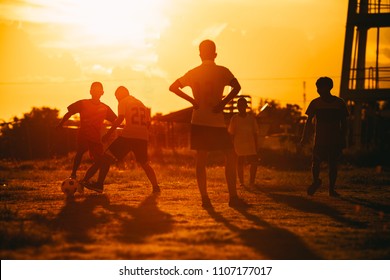 An action sport picture of a group of kids playing soccer football for exercise in community rural area under the sunset.