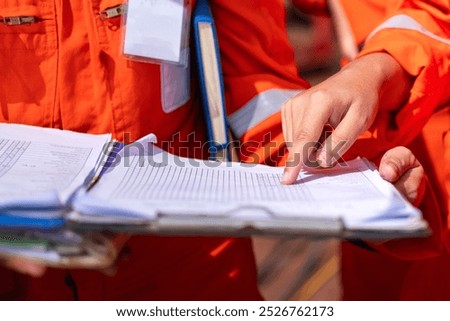 Action of a supervisor is checking on paperwork document during perform safety audit at operation work site. Industrial working scene, close-up and selective focus.