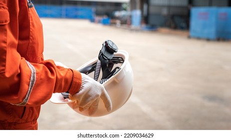 Action of a worker is preparing to wear a white safety hardhat with blurred background of factory workplace. Industrial safe work practice concept photo, selective focus.